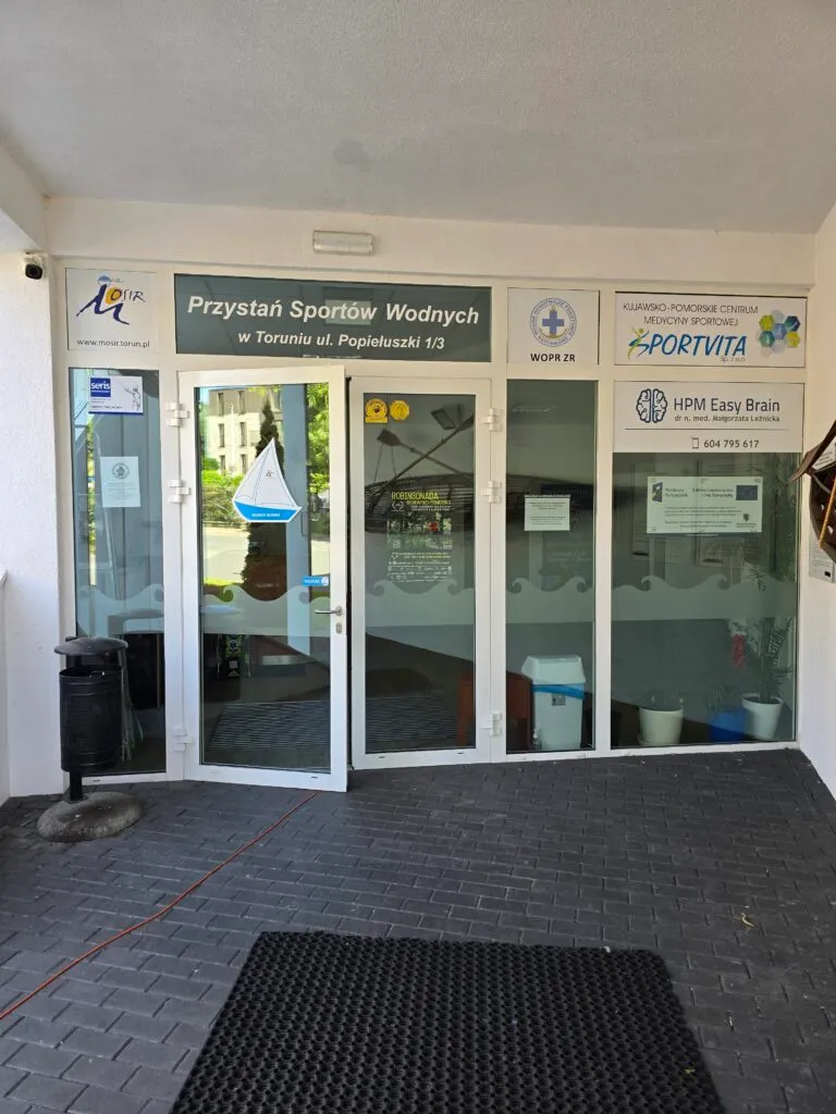 Wejście do Przystani Sportów Wodnych przy ul. Popiełuszki w Toruniu z oznaczeniem WOPR i plakatem projektu na szybie