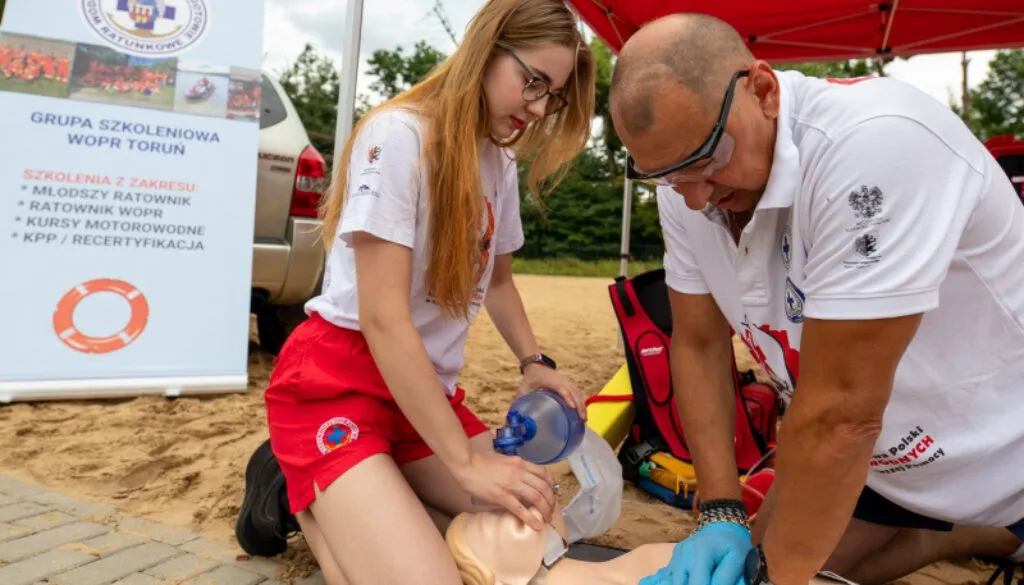Ratowniczka i instruktor WOPR ćwiczą resuscytację na fantomie na plaży