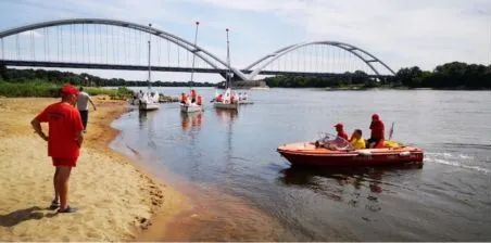 Ratownik WOPR na plaży nad Wisłą w Toruniu, w tle łódź ratownicza i most